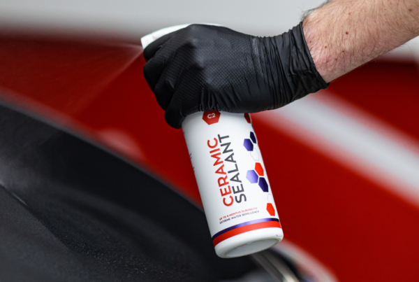 A person wearing black gloves sprays car polish onto a vehicle's surface.