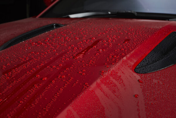 water droplets rolling off red car closeup on hood